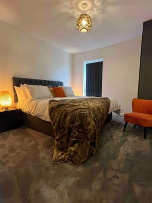 A modern hotel room with a large bed, a nightstand with a lamp, a chair, and a ceiling light fixture.