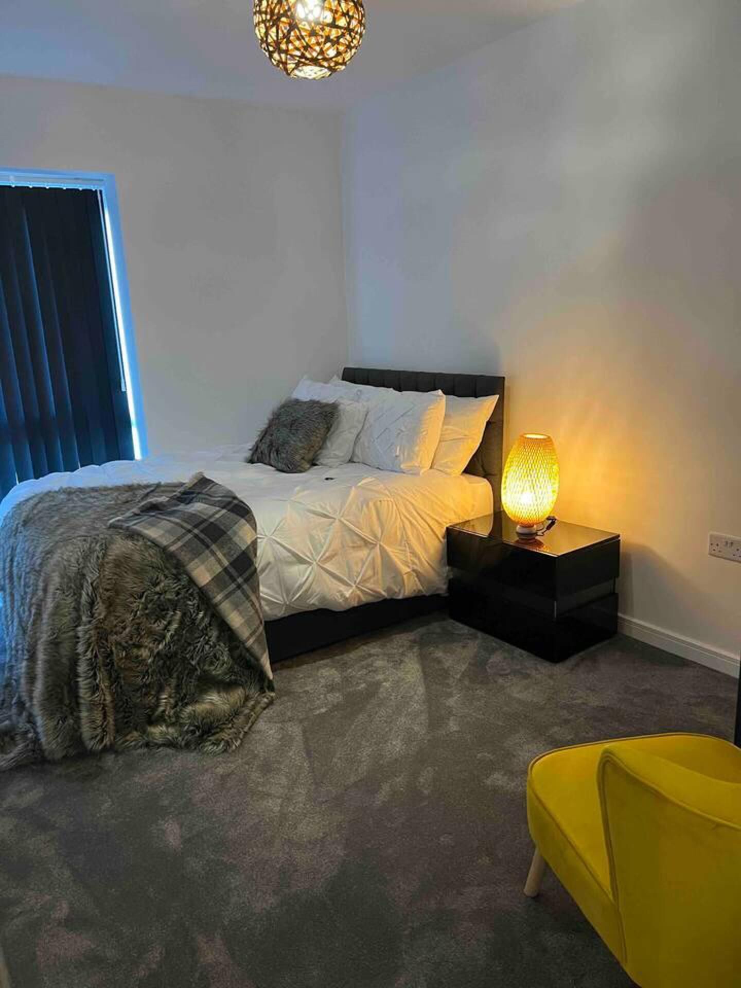 Un dormitorio con cama, mesita de noche, lámpara y una silla.