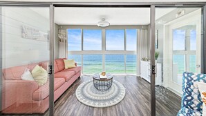 Un salon spacieux avec une grande fenêtre donnant sur l’océan, un canapé rose, une table basse ronde et une vue sur la plage.