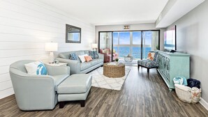 Un salon moderne avec vue sur l’océan, comprenant un canapé bleu clair, un fauteuil rose et un meuble turquoise.
