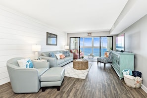 Sala de estar moderna com vista para o oceano, com um sofá azul claro, uma poltrona rosa e um armário verde-água.