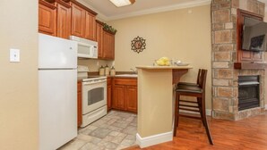 Een keuken met houten kasten, een witte koelkast, een fornuis, een spoelbak en een stenen openhaard.