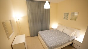 Ein Schlafzimmer mit einem Bett, Nachttischen, einem Spiegel und einem Fenster mit Vorhängen.