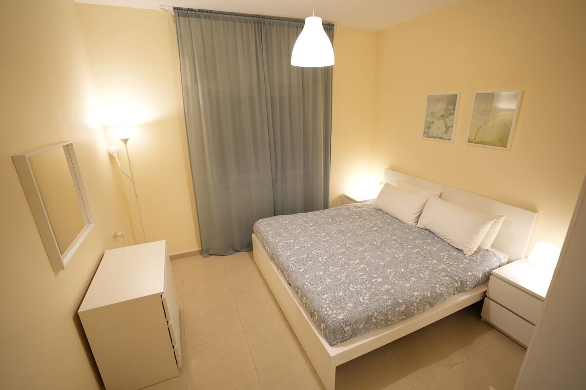 A bedroom with a bed, bedside tables, a mirror, and a window with curtains.