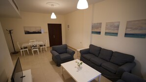 Ein Wohnzimmer mit einem weißen Couchtisch, zwei grauen Sofas, einem weißen Esstisch mit Stühlen und einem Schuhregal.