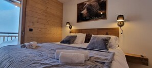 A cozy bedroom with a wooden headboard, a large bed with multiple pillows, and a mounted picture of a bear. - 4th floor, balcony, tv, 82m², La Plagne (Aime)