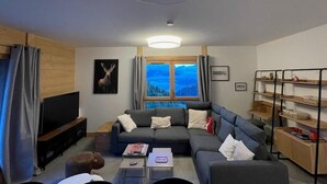 Ein modernes Wohnzimmer mit einer Couch, einem Fernseher und einem Fenster mit Bergblick.