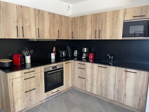 A modern kitchen with wooden cabinets, a black countertop, and stainless steel appliances including a Bosch microwave and oven. - 4th floor, balcony, tv, 82m², La Plagne (Aime)