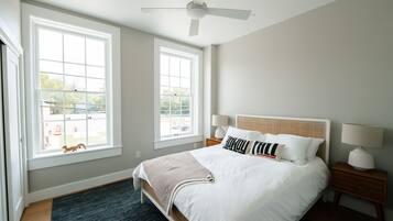 Quarto com uma cama grande, duas mesas de cabeceira, um ventilador de teto e duas janelas.