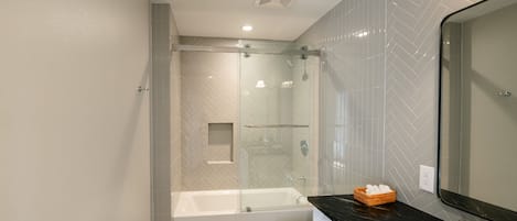 A modern bathroom with a glass-enclosed shower, a white toilet, and a black countertop with a mirror.