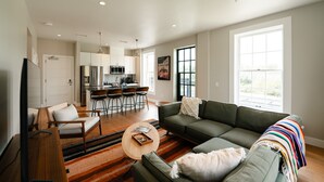 Ein modernes Wohnzimmer mit einer Couch, einem Couchtisch und einem Essbereich mit Stühlen, im Hintergrund eine Küche.