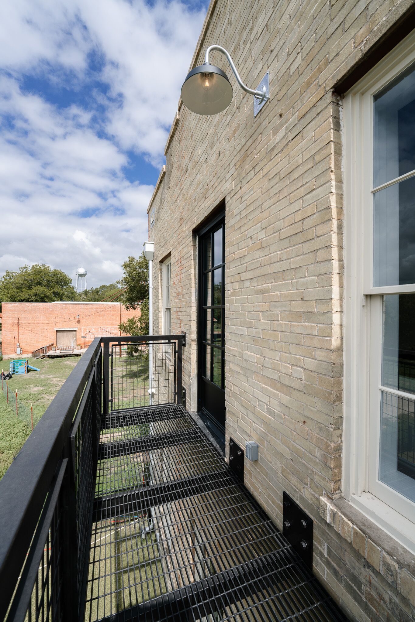 A brick building with a metal balcony, a water tower in the background, and a clear sky.