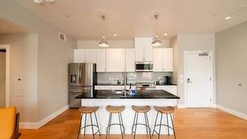 A modern kitchen with white cabinets, stainless steel appliances, and a central island with bar stools.