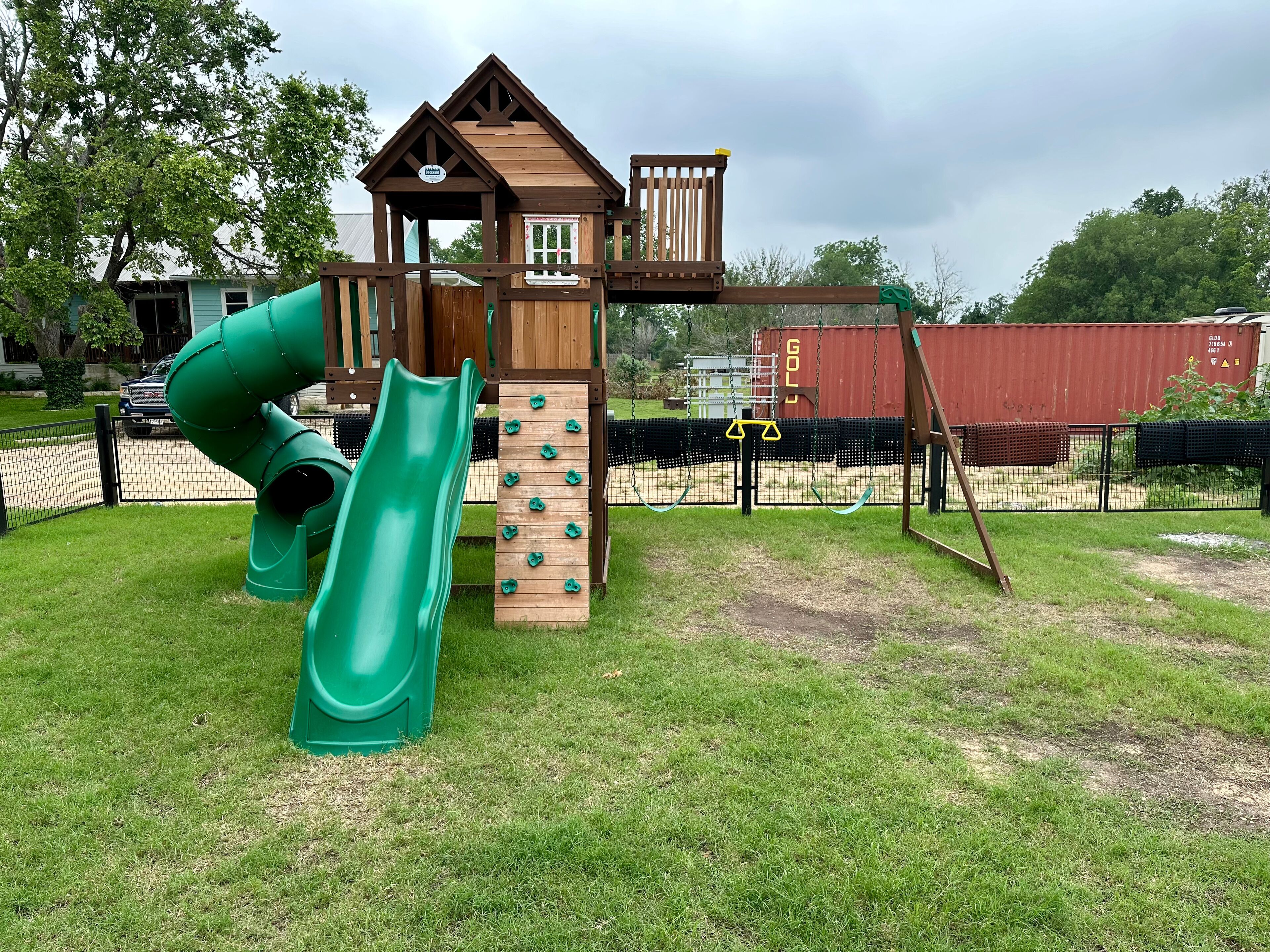 Un parque infantil con tobogán, pared de escalada y una casita de madera.