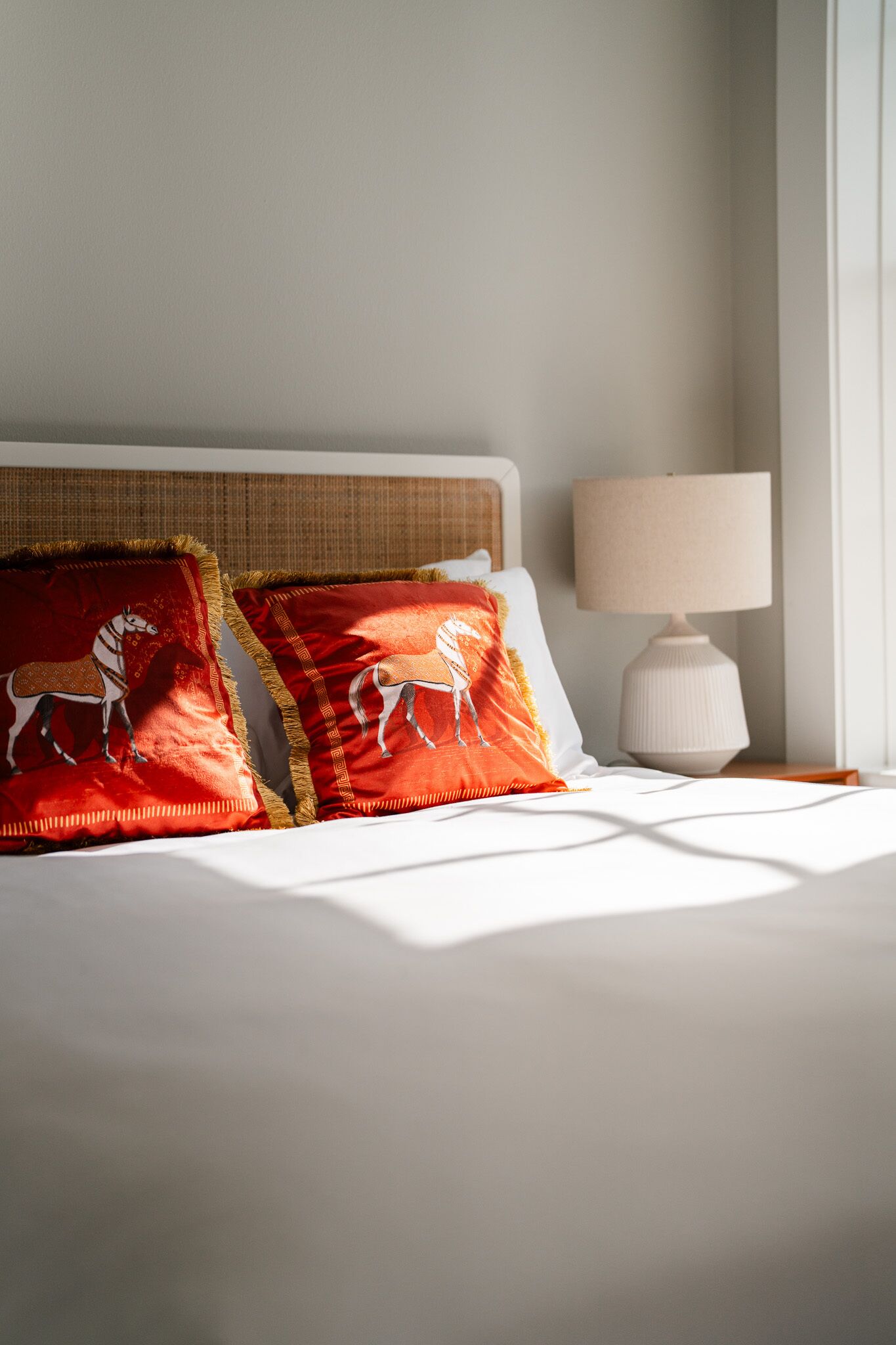 Een net opgemaakt bed met witte lakens en twee rode kussens met paardenmotieven.