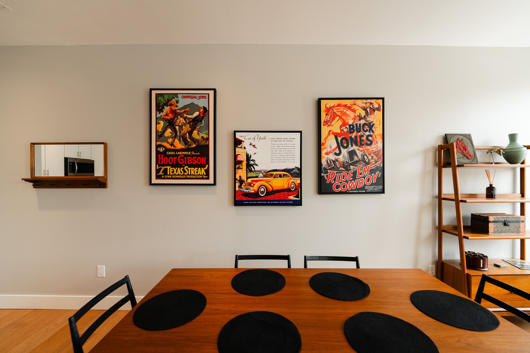 Ein Essbereich mit Holztisch, schwarzen Platzsets und drei Vintage-Filmplakaten an der Wand.