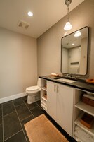 A modern bathroom with a white toilet, a black countertop, a mirror, and a black and white tiled floor.