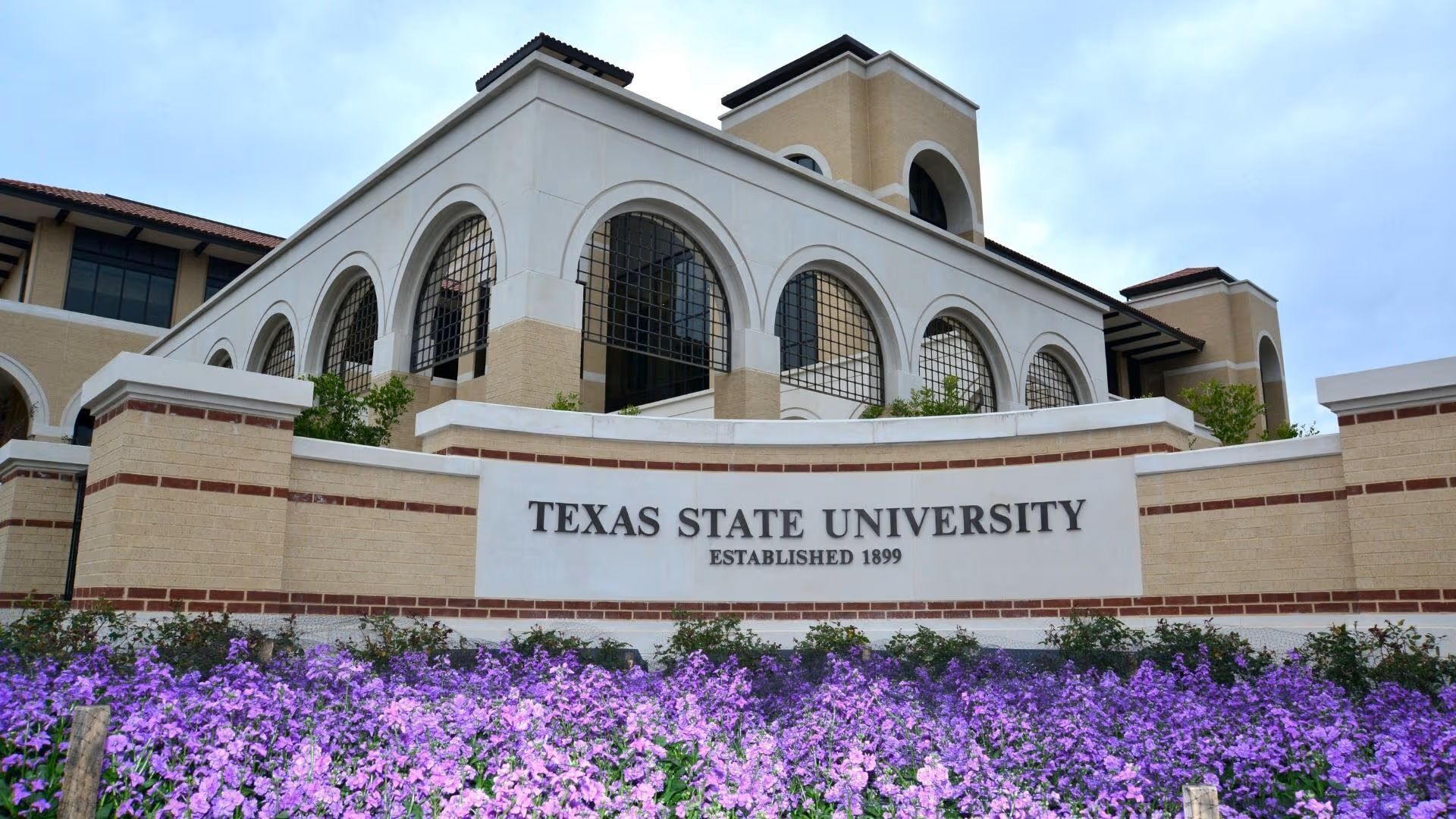 Texas State University building with arched windows and a sign stating its establishment year.