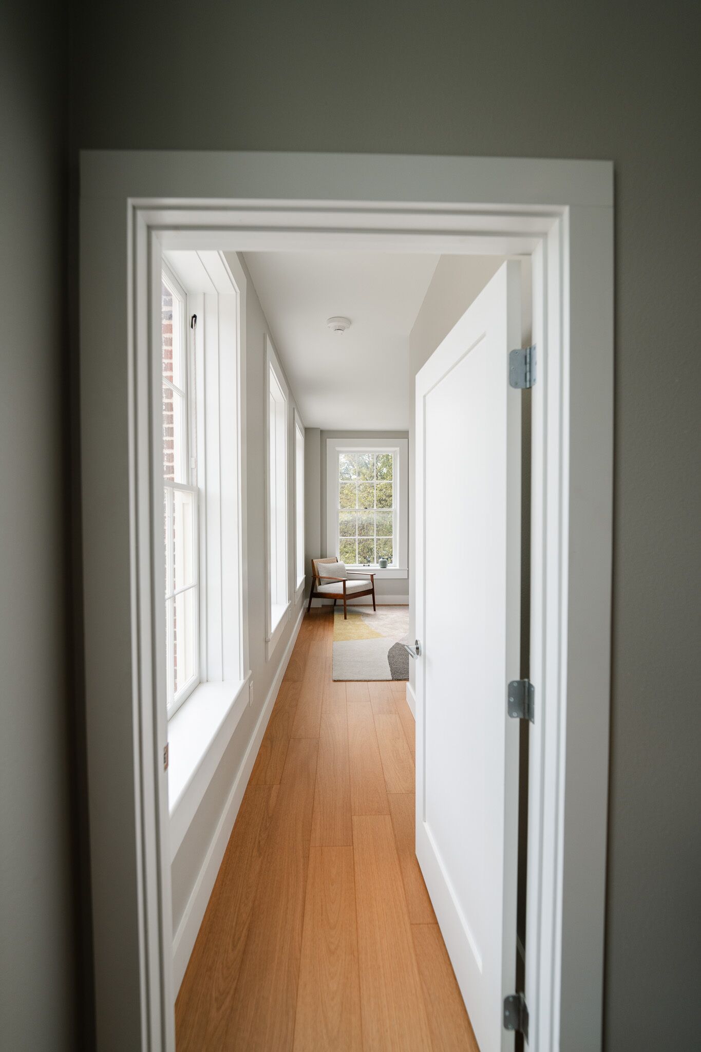Un couloir doté d’un plancher en bois, de murs blancs et de grandes fenêtres.