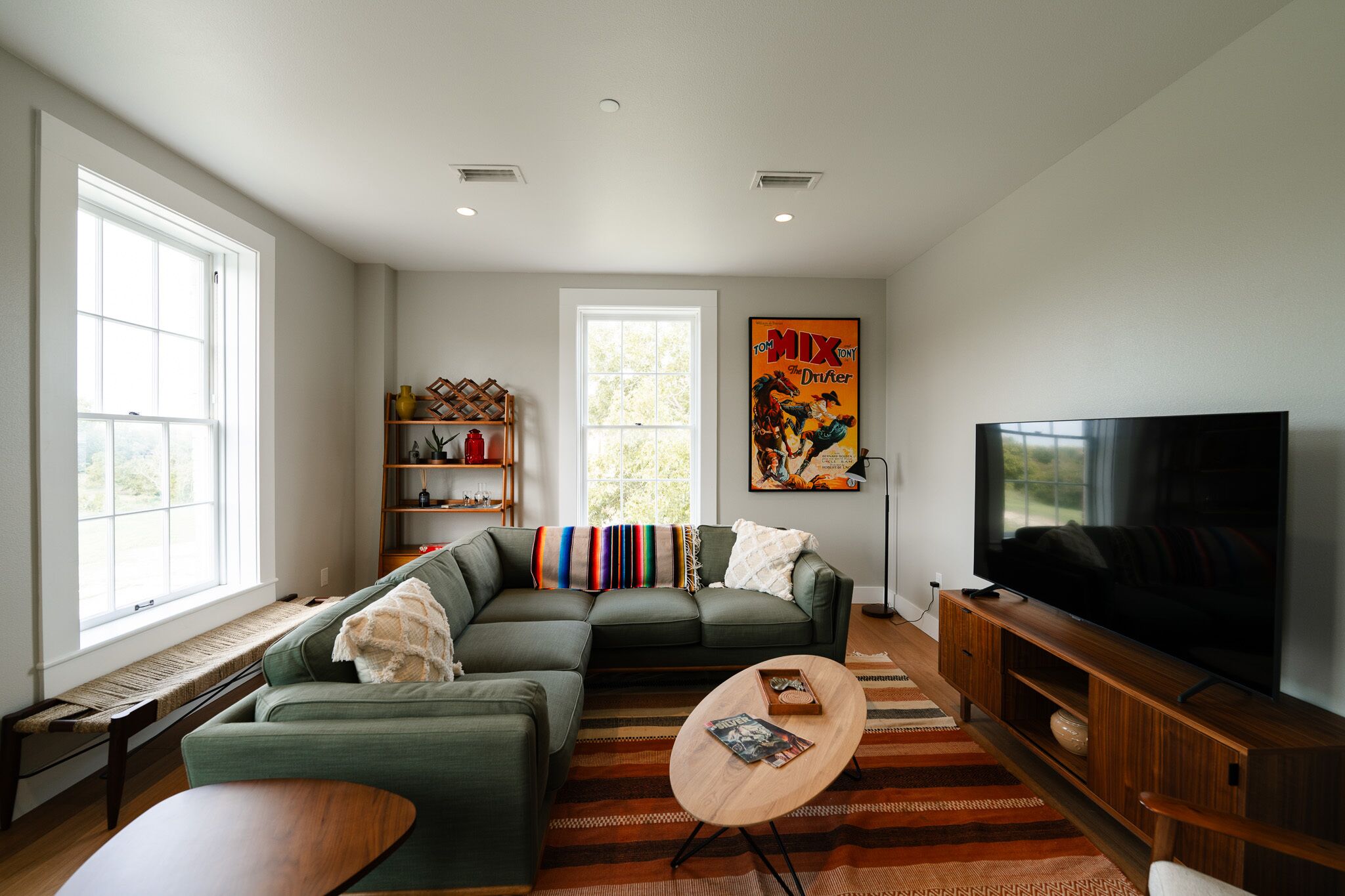 A modern living room with a sectional sofa, a flat-screen TV, a wooden coffee table, and a bookshelf.