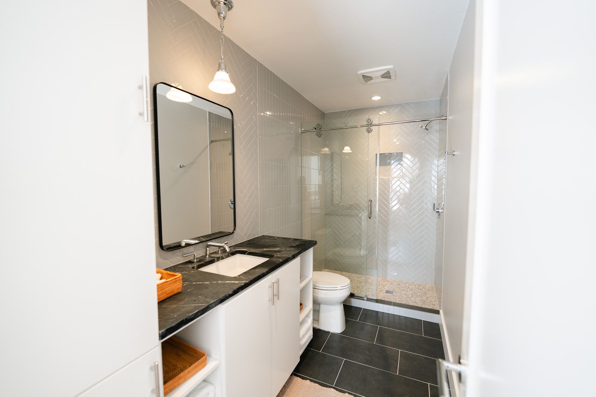 A modern bathroom with a glass-enclosed shower, a white sink with a black countertop, and a large mirror.