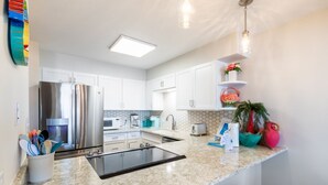 A modern kitchen with white cabinets, a stainless steel refrigerator, a granite countertop, and a built-in island.