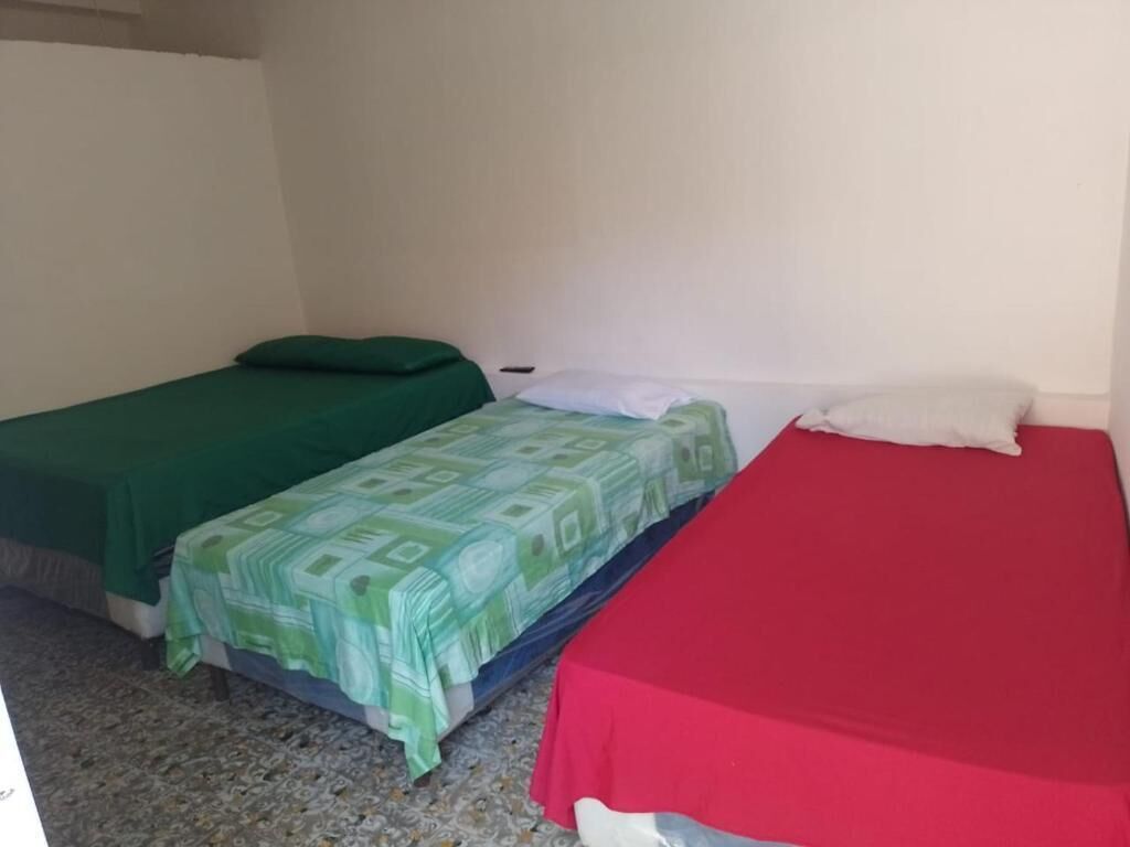 Two single beds with green and red bedspreads in a room with plain white walls and a patterned floor.