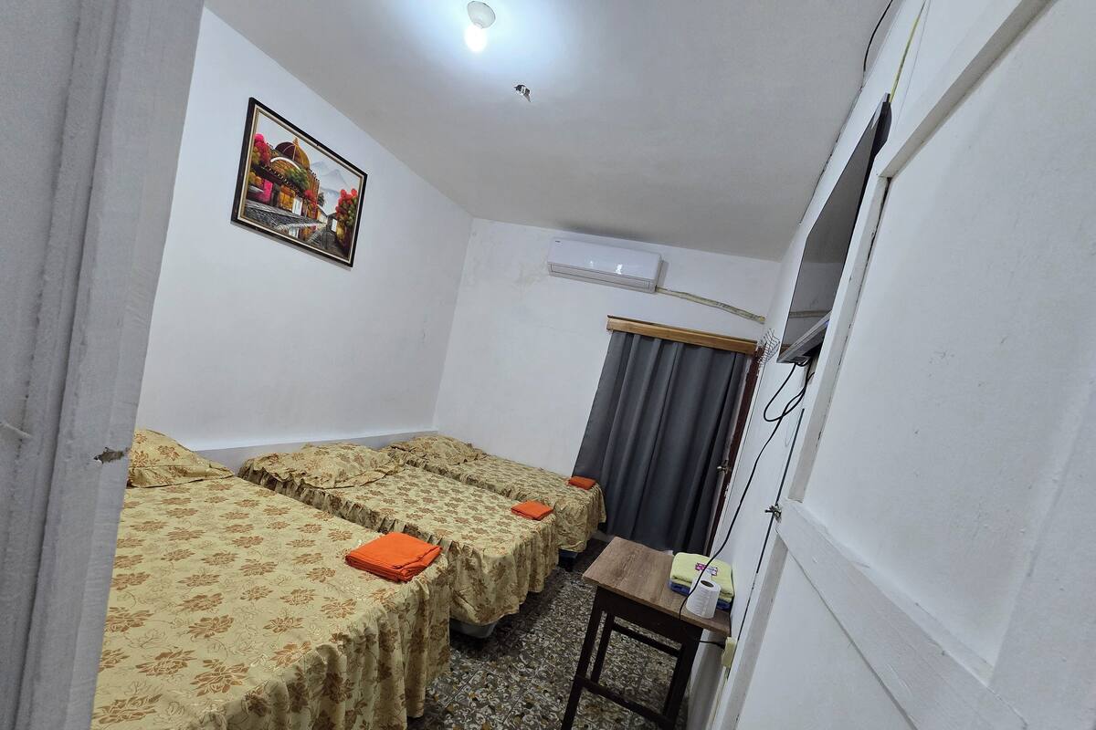 A small, compact room with two single beds, a small table, a curtain, and a ceiling light.