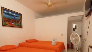 A room with two beds covered in orange sheets, a ceiling fan, a painting on the wall, and a television mounted on the wall. - Hotel Villa Aurora (Flores)