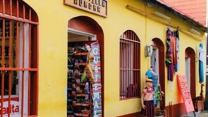 A storefront with a yellow facade, a sign reading "HOLA CORRIDO", and various items displayed outside, including a colorful sign with "GUA" visible. - Hotel Villa Aurora (Flores)