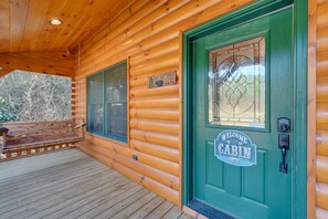 A cabin entrance with a green door, a welcome sign, and a bench outside.