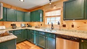 A kitchen with green cabinets, granite countertops, and wooden flooring. - On-Site Waterfall! Cabin Near Blue Ridge Pkwy (Ennice)