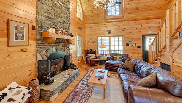 A cozy log cabin interior with a stone fireplace, leather sofa, and a chandelier. - On-Site Waterfall! Cabin Near Blue Ridge Pkwy (Ennice)