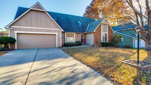 A single-story house with a garage, a front yard with fallen leaves, and a tree with autumn foliage. - Overland Park Family Home w/ Game Room & Backyard! (Overland Park)