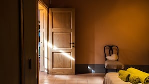 Una habitación de hotel con una puerta de madera, una silla con cojín y una cama con toallas amarillas.
