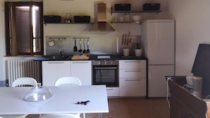 Una cocina compacta con armarios blancos, estufa, refrigerador y una mesa de comedor con sillas.