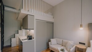 A compact living space with a kitchenette, a white sofa, and a small table. - San Rocco Suite #3 by Corfu Collection
 (Kerkira)