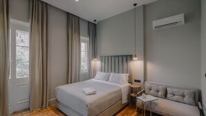 Une chambre moderne avec un grand lit, un canapé, une petite table et un appareil de climatisation.