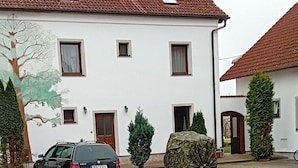 A courtyard with a paved area, a parked car, and a white building with a red-tiled roof. - Pension u Dubu (Frantiskovy Lazne)