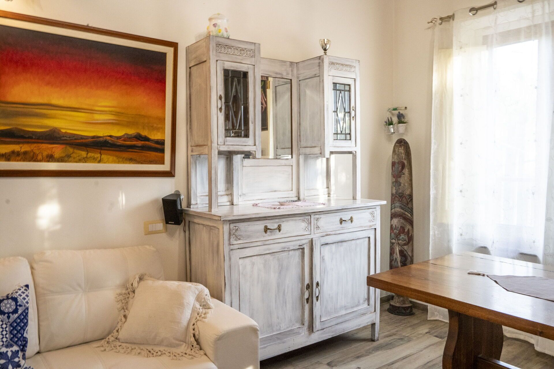 Una habitación con un sofá blanco, una mesa de comedor de madera y un armario blanco con puertas de vidrio.