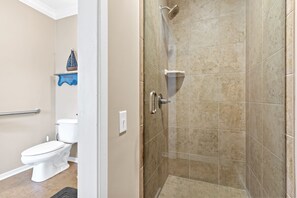 A bathroom with a toilet, a shower, and a shelf with a decorative item.