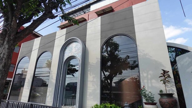 A building with three large arched windows, a metal railing in front, and potted plants on the ground. - RTW Residence (Bangkok)