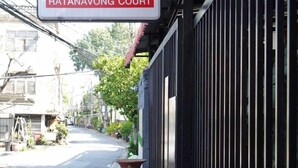 A sign for Ratanavong Court, a building with a black metal fence and potted plants on the sidewalk. - RTW Residence (Bangkok)