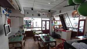 A restaurant with wooden tables and chairs, a counter with a cash register, and a staircase leading to an upper level. - RTW Residence (Bangkok)