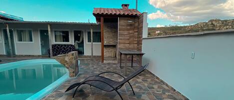 A rooftop pool area with lounge chairs, a small wooden structure, and a clear blue sky.