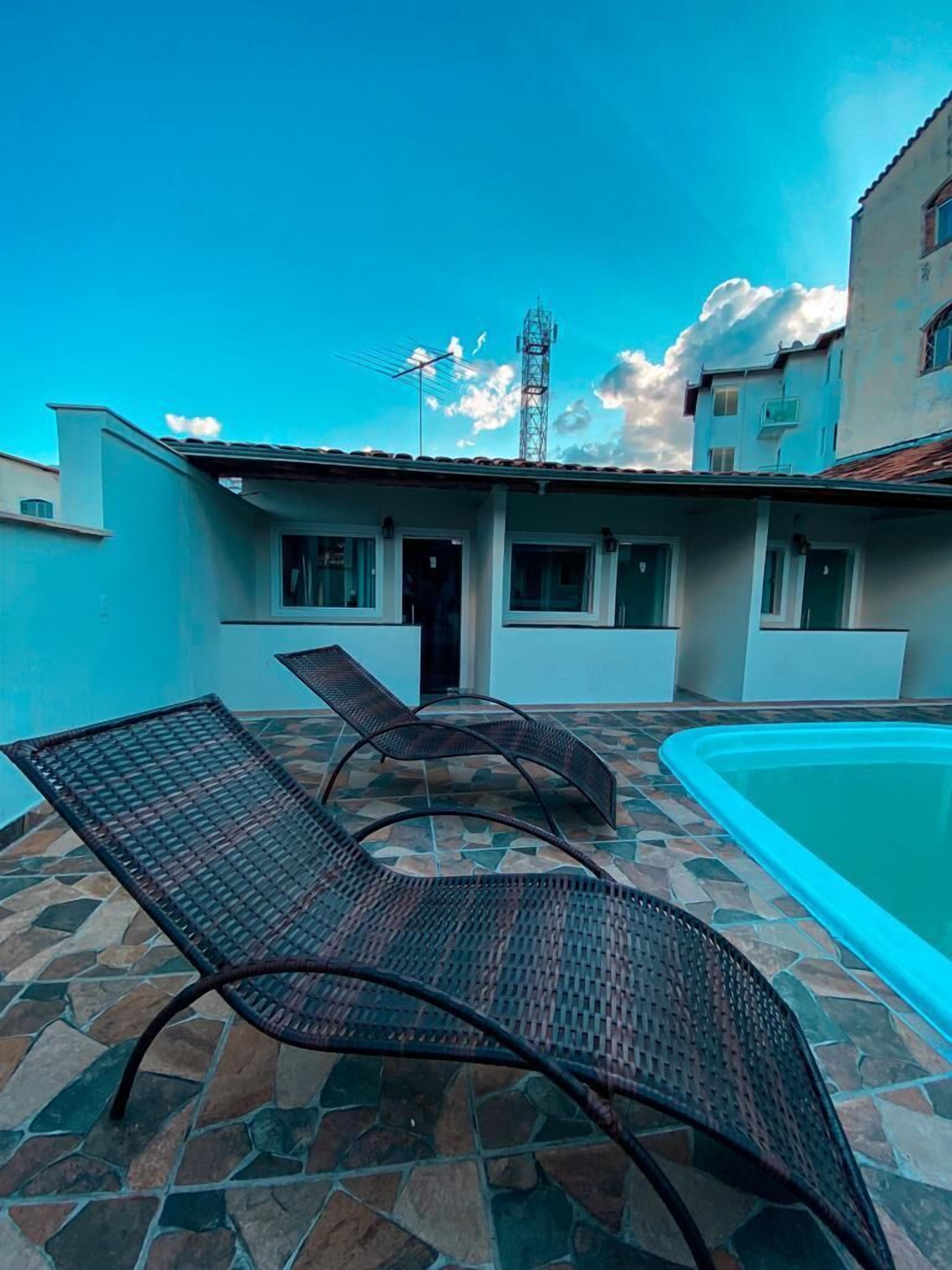 A courtyard with a swimming pool, two lounge chairs, and a building with multiple windows and a door.
