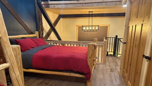 A loft-style bedroom with a wooden bed, a red blanket, and a wooden headboard. - Oz Lodge: Tiehacker Chalet.

 (Seward)
