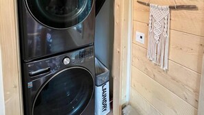 A compact laundry room with two stacked front-loading washing machines, a small trash bin, and a macramé wall hanging. - Oz Lodge: Tiehacker Chalet.

 (Seward)