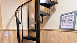 A spiral staircase with a black metal frame, a wooden bench with storage underneath, and a wall-mounted sign with text. - Oz Lodge: Tiehacker Chalet.

 (Seward)