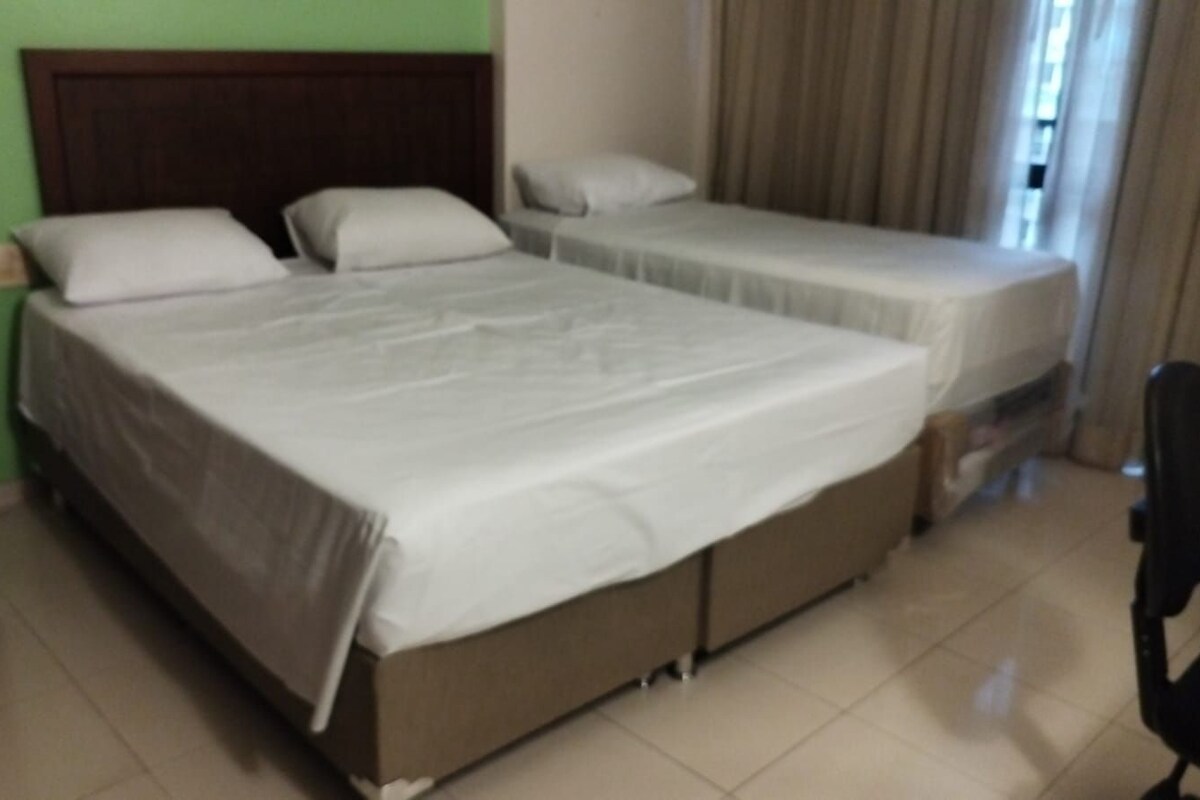 Una habitación de hotel con dos camas, una mesita de noche, una silla y un ventanal con cortinas.